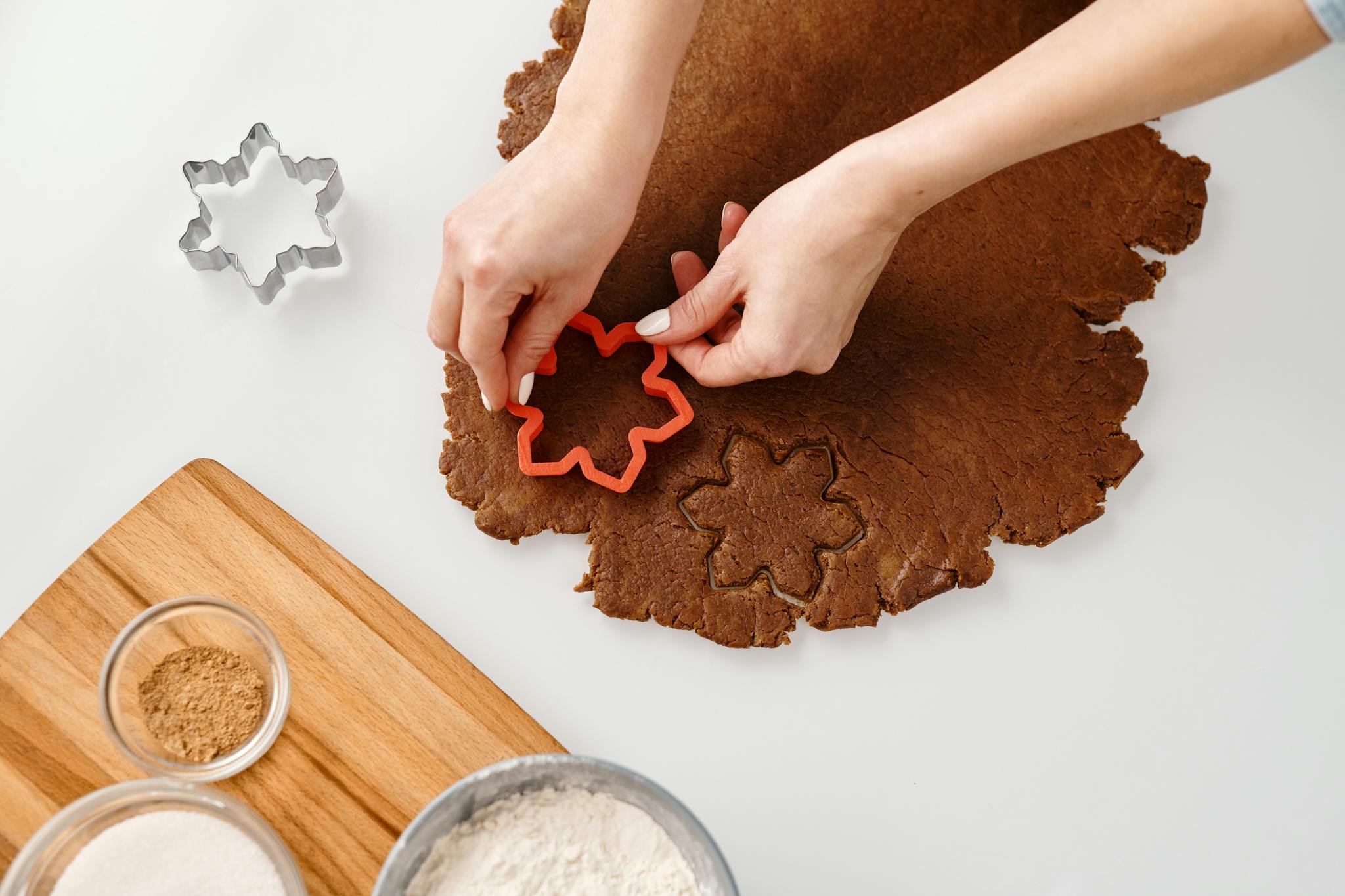 Hands using snowflake cutters to shape holiday cookies from chocolate dough in a cozy kitchen setting.